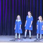 Muzikinis festivalis-konkursas "Muzikoje - mes šeima" trys mergaitės su mėlynomis suknelėmis koncertuoja