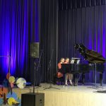 Muzikinis festivalis-konkursas "Muzikoje - mes šeima" dvi raudonai apsirengusios mergaitės groja pianinu